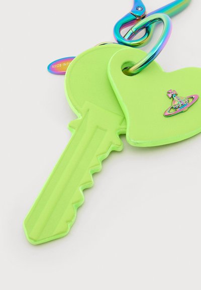 Svetlozelený kľúč a prívesok v tvare srdca pripevnené na dúhovo sfarbenom kovovom klipu s perleťovým efektom na bielom pozadí.