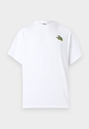 Person mit dunklem lockigem Haar und Vitiligo, die ein weißes T-Shirt trägt, das eine grüne Apfel-Grafik und den Text "THE NORTH FACE" auf der Rückseite zeigt.