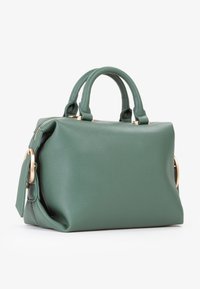 Borsa a tracolla in pelle verde con texture, dotata di doppi manici, zip in tonalità oro e dettaglio della chiusura laterale, posizionata su uno sfondo bianco.