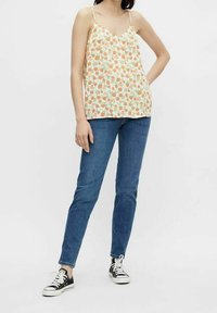 Lätt, krämfärgad linne med orange och grönt blommönster. Kombinerad med mörkblå tajta jeans och svarta sneakers. Spagettibiräknade.