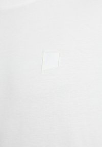 Weißes Baumwoll-T-Shirt mit einem kleinen, strukturierten, gestickten, dreieckigen Logo in dezenten Tönen. Weiches Gewebe mit glatter Oberfläche.