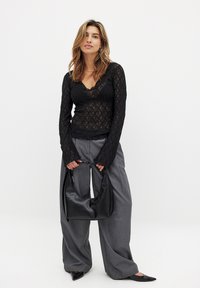 Black lace long-sleeve top with a v-neck, paired with gray loose-fitting trousers. Holding a black leather hobo bag.