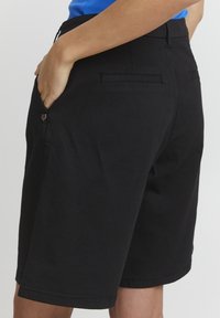 Svarta bomullsshorts med rak skärning, med sidofickor och en sydd fåll. Inga synliga mönster eller metallaccenter.