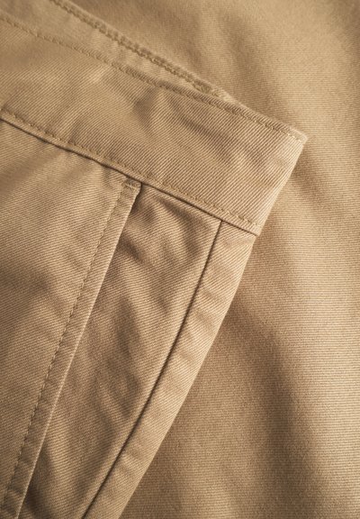 Primo piano di un tessuto beige con una texture liscia, caratterizzato da un orlo piegato e dettagli cuciti, che mette in risalto un design minimalista.