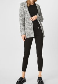 Blazer gris texturé avec des accents noirs ; porté sur un haut noir et un pantalon noir ajusté ; complété par des chaussures noires avec un détail en métal.