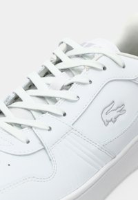 Baskets en cuir blanc avec lacets blancs, panneaux cousus et logo crocodile embossé sur le côté.