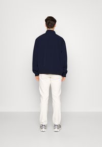 Mornarsko modra sweatshirt s stoječim ovratnikom, rebrastimi manšetami in spodnjim robom, v kombinaciji z belimi hlačami in sivimi športnimi čevlji. Preprost, sproščen dizajn.