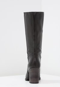 Botte noire en cuir montant jusqu'au genou avec un bout arrondi, une texture lisse, des coutures verticales et un talon en bois empilé.