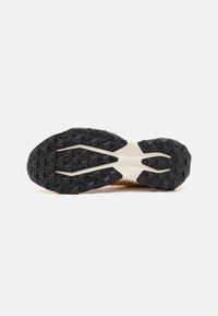 Semelle extérieure en caoutchouc noir avec un motif de bande de roulement triangulaire, semelle intermédiaire crème et tige lisse en marron. Détails sculptés notables sur le caoutchouc.