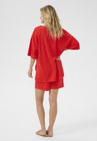Piros loungewear szett, amely egy túlméretezett, rövidujjú felsőből és hozzá illő sortból áll. Puha anyag, lazán illeszkedő szabás, minimalista kialakítás.