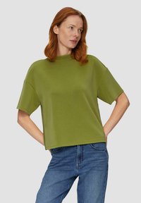 Olivgrüner kurzärmliger Pullover mit hohem Kragen, lockerer Passform und weicher Stofftextur, kombiniert mit blauen Jeanshosen.