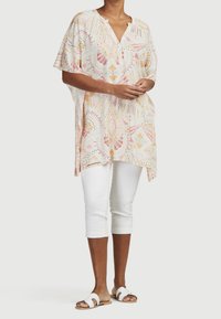 Lätt, mönstrad tunika i pastellfärger med geometriska mönster. Har en V-ringning och korta, vida ärmar, kombinerad med vita capris.