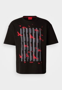 Schwarzes Baumwoll-T-Shirt mit einem grafischen Design aus sich überlappenden grauen Linien und roten Vögeln. Logo in Rot am unteren Rand. Lässige, lockere Passform.