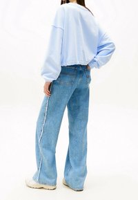 Sudadera cortada de color azul claro con mangas abullonadas, combinada con jeans azules de cintura alta que tienen costuras laterales deshilachadas y un ajuste relajado.