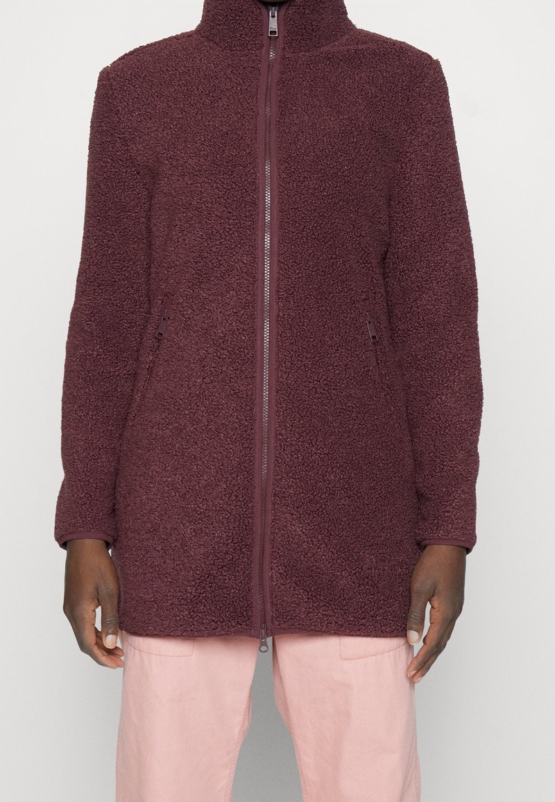 Fleecová bunda v barvě bordó s vysokým límcem, celým zipem a bočními kapsami. Má strukturovanou, měkkou tkaninu a elastické manžety.