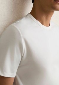 Balta trumpa rankovė t-shirt marškiniai, pagaminti iš lygios, minkštos medžiagos; turi klasikinį apvalų kaklo iškirpimą ir prigludusį siluetą. Subtili tekstūra ir švarios linijos.
