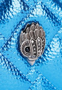 Sac en cuir métallique bleu avec une surface texturée, des détails en motif diamant et un accent en métal argenté orné ressemblant à un motif floral.