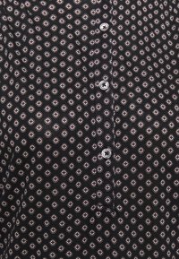 Camicia nera con un motivo ripetuto di piccoli diamanti chiari, con chiusura a bottoni e dettagli in bottoni argentati.