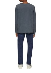 Chemise grise à manches longues avec une coupe décontractée, texture douce et col rond classique, associée à un jean bleu foncé et des baskets blanches.