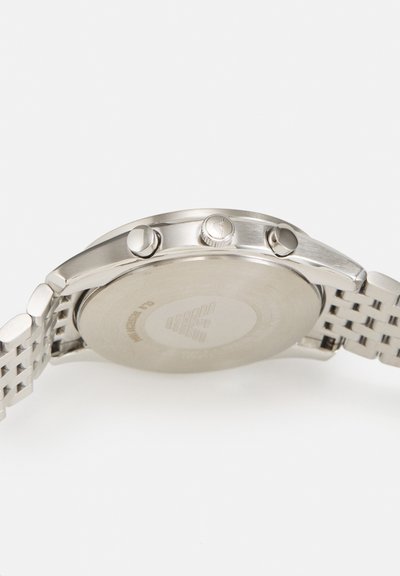 Rückseite einer silbernen Metallarmbanduhr mit zwei Drückern und einer Krone an der Seite, verbunden mit einem silbernen Metallarmband.