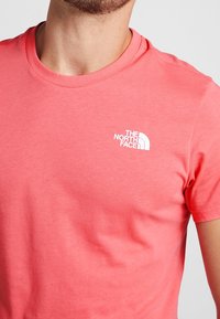 Coral short-sleeve t-shirt made of soft cotton; features a white logo of The North Face on the left chest area. Smooth texture.