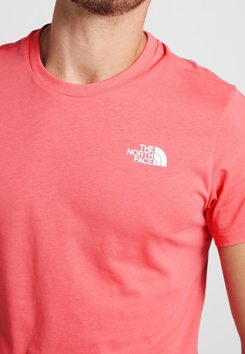 Coral short-sleeve t-shirt made of soft cotton; features a white logo of The North Face on the left chest area. Smooth texture.