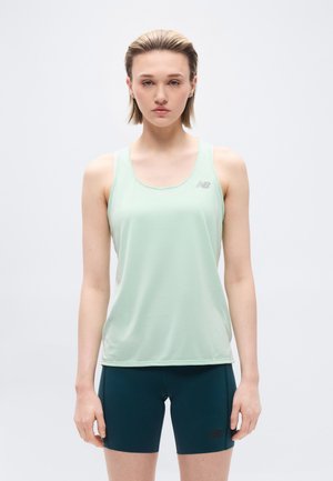 Ung person med kort hår iført lys grønn ermeløs trenings-topp og mørkeblå tettsittende shorts mot en ensfarget hvit bakgrunn.