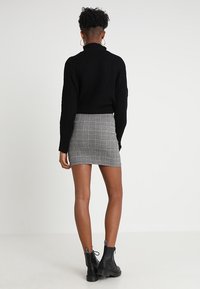 Pull en noir à côtes avec un col montant, associé à une jupe grise à carreaux ajustée. Des bottines noires viennent compléter la tenue.