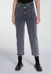 Jeans in denim nero sbiadito a vita alta con orli sfrangiati, abbinati a una cintura nera borchiata, indossati con calzini neri e mocassini.