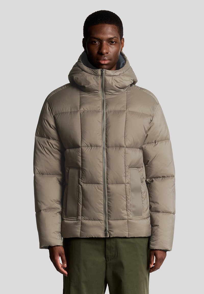 Lichtbruine pufferjack met capuchon, voorzien van een quilted ontwerp, een rits aan de voorkant en zijzakken. De textuur is soepel en gewatteerd.