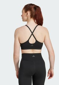 Sujetador deportivo negro con tirantes cruzados y detalle de logotipo, combinado con leggings negros de tiro alto que presentan costuras elegantes y un acento de logotipo.