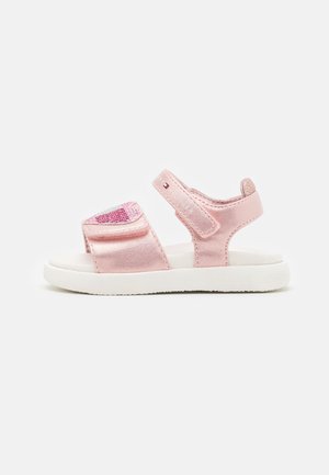 Sandale rose pour tout-petit avec semelle blanche, deux brides réglables et un petit logo drapeau sur la bride latérale, présentée sur fond blanc.