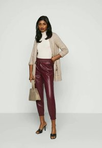 Beige cardigan, white turtleneck, and burgundy faux leather pants. Black open-toe heels and a textured beige handbag complete the outfit.