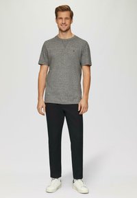 T-shirt gris à manches courtes avec une finition texturée, associé à un pantalon noir ajusté et des baskets blanches. Détail de logo discret sur le t-shirt.