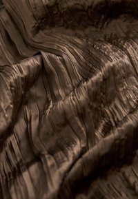 Tissu plissé marron à texture soyeuse, présentant des lignes ondulées horizontales et un éclat subtil, créant un aspect superposé.