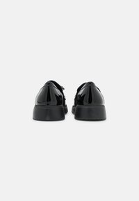 Chaussures noires en cuir verni avec un bout rond, une texture lisse et une semelle épaisse et basse. Présentent un laçage simple et un design épuré.