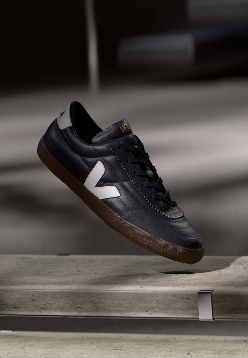 Adidași din piele neagră cu logo alb în formă de V, cu șireturi pe față, detalii perforate și talpă din cauciuc maro; design elegant cu accente minime.