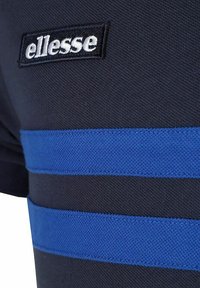 Czarna koszulka sportowa z niebieskimi poziomymi paskami i haftowanym białym logo "ellesse" po lewej stronie. Teksturowana struktura materiału.