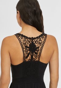 Schwarzes Kleid mit einem Spitzenrücken-Design und floralen Mustern sowie aufwendigen Nähten, tailliertem Oberteil und fließendem Rock.