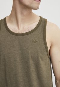 Olivgrünes Tanktop aus einem weichen, strukturierten Stoff. Verfügt über einen runden Halsausschnitt und ein dezentes, eingeprägtes Logo auf der Brust.