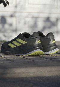 Czarne buty sportowe z limonkowymi akcentami i trzema paskami po bokach. Wykonane z teksturowanego materiału i mają kontrastującą jasnoszaro midsole.