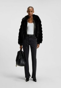 Giacca bomber in pelliccia sintetica nera con colletto ampio, abbinata a un top bianco a coste, jeans neri a vita alta e una borsa nera con cordino.