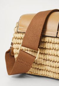 Woven straw bag with a tan leather flap and brown fabric strap. Features gold hardware and visible stitching details. Compact rectangular shape.