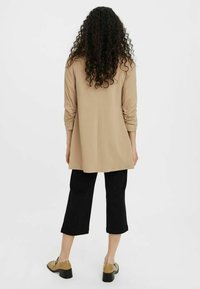 Maglietta beige a maniche lunghe con design dritto, abbinata a pantaloni cropped neri e scarpe con tacco beige chiaro, vista da dietro.