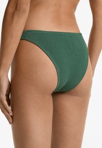 Parte inferiore di bikini verde realizzata in tessuto testurizzato, con taglio a vita bassa e copertura minimale, caratterizzata da bordi lisci e vestibilità sagomata.
