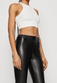 Un haut court blanc à col montant et emmanchures larges, associé à un pantalon ajusté noir en simili cuir avec une texture lisse.