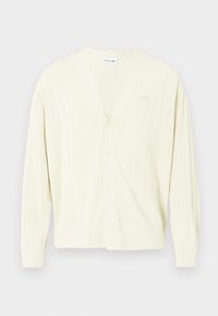 Ανοιχτό κίτρινο καρντιγκάν, ριγωτή υφή, V-λαιμόκοψη, κλείσιμο με κουμπιά, μακριά μανίκια, με μια διακριτική λογότυπη επιγραφή στο στήθος. Μαλακό, πλεκτό υλικό.