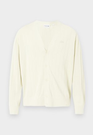 Cardigan jaune clair, texture côtelée, col en V, fermeture à boutons, manches longues, avec un logo subtil sur la poitrine. Matière douce et tricotée.