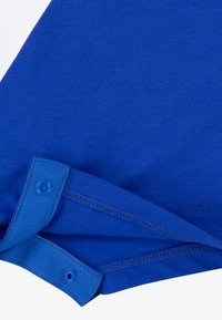 Blå bomullsstoff med myk tekstur, med brettet kant og knappedetaljer. Sydd kant og glatt finish er synlig.