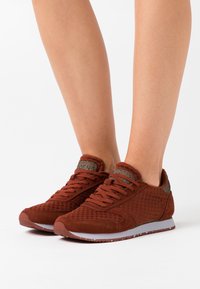 Red athletic shoes made of textured mesh and suede with a padded collar, featuring a grey midsole and matching laces.